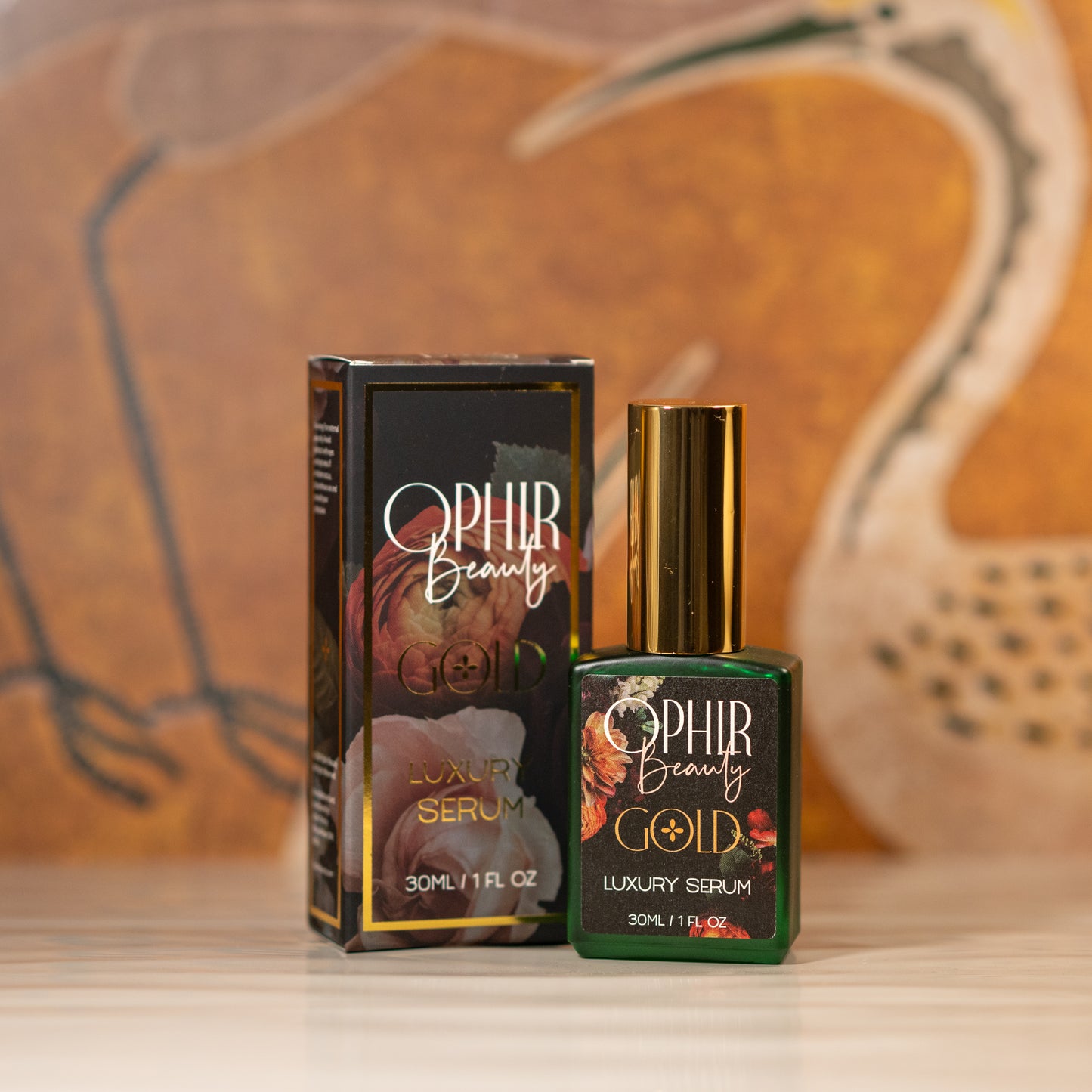 A green glass bottle of Ophir Gold Walnut oil serum stands beside its black and gold retail box on wavy white tiles, with vintage crane wallpaper in the background.