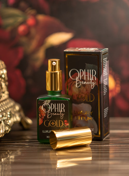 A bottle of Ophir Gold Serum, uncapped to show its pump dispenser, stands beside an ornate golden telephone, with rich red florals and berries in the background