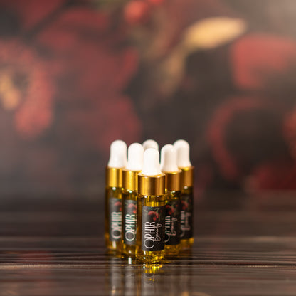 angled view of several small glass dropper bottles filled with golden oil serum, arranged in a pyramid on a wavy bronze surface, with dark hazy florals in the background.