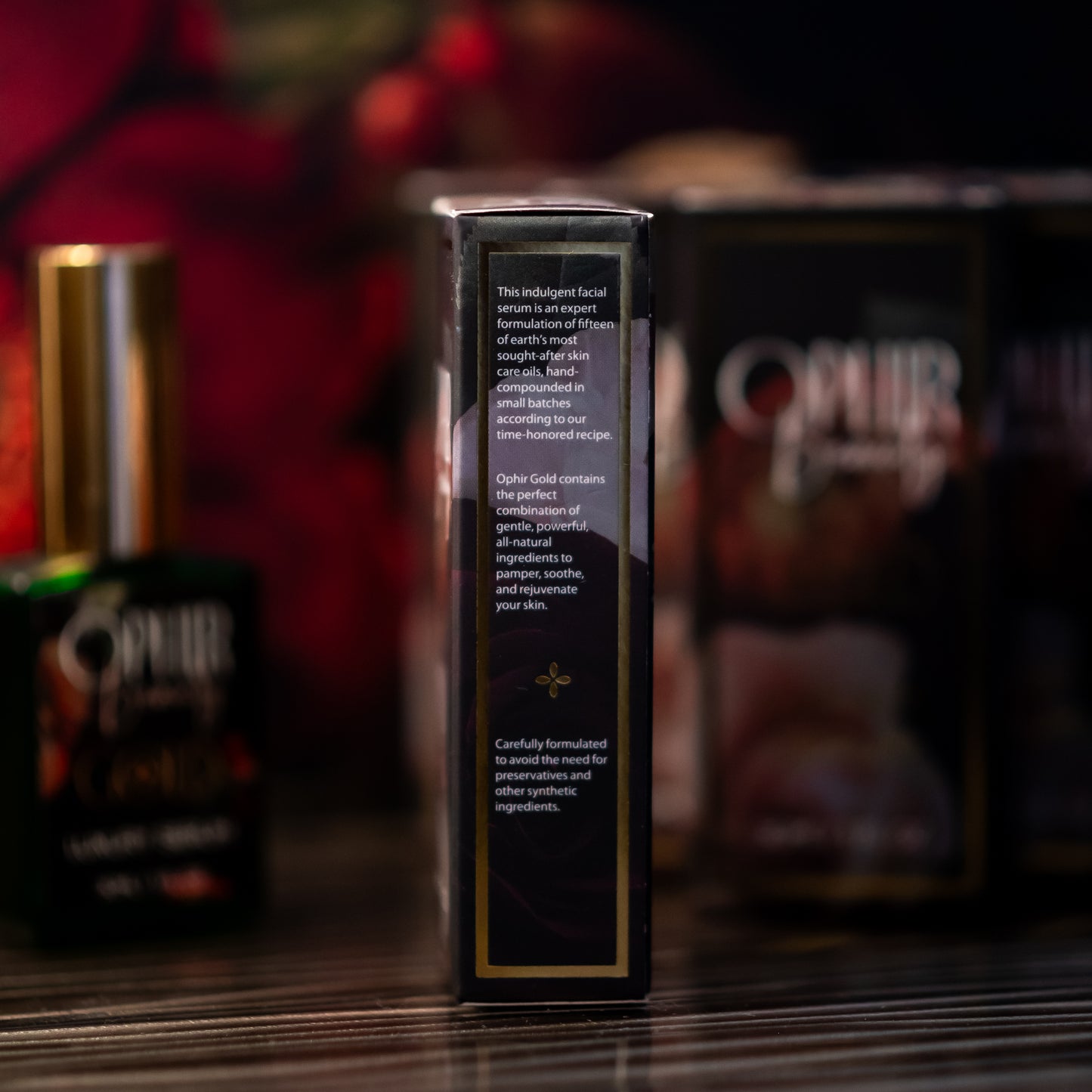 closeup of the side panel of Ophir Gold Argan oil serum's retail box, showing its description, with a glamorous dark floral background.